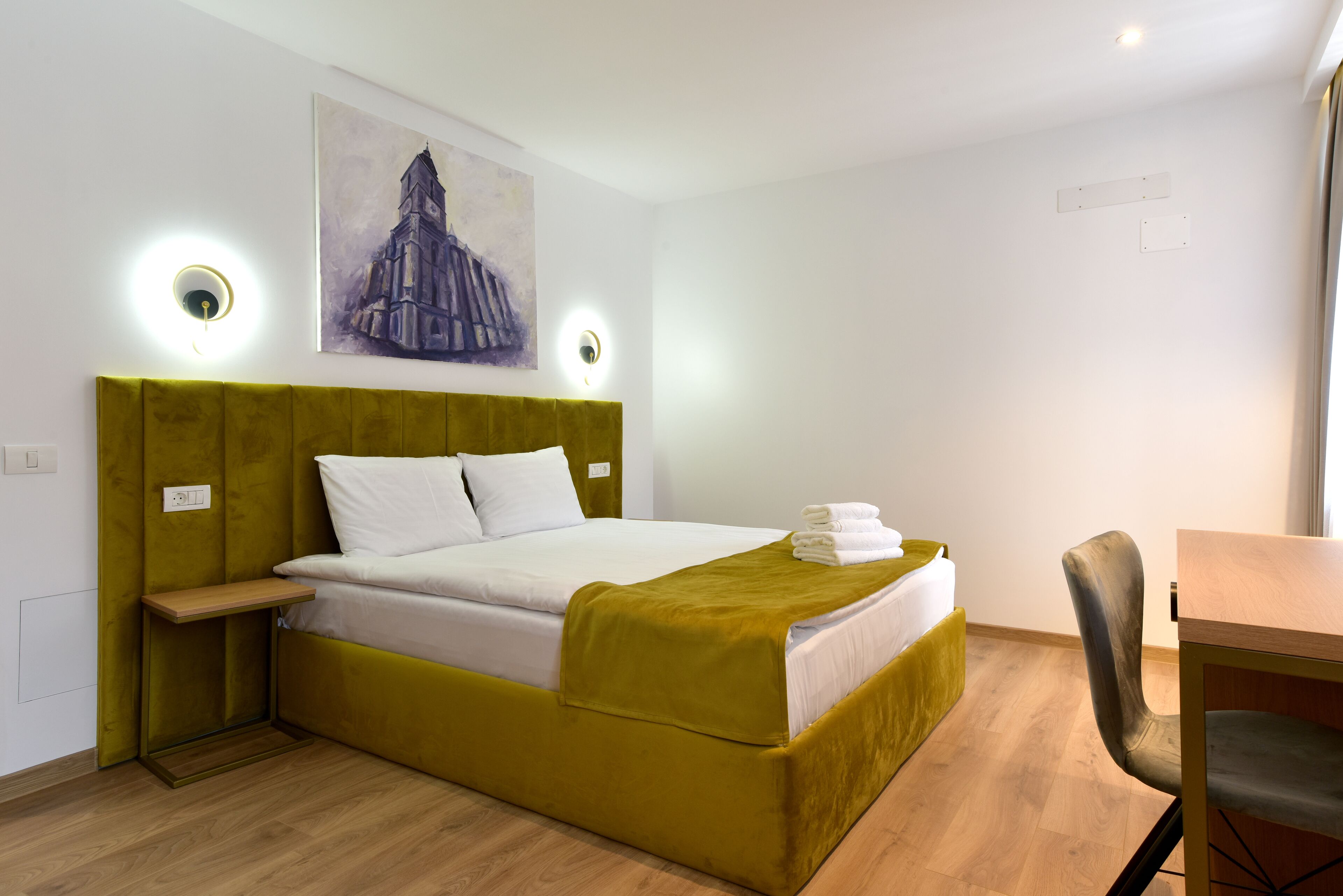 A hotel room with a large bed, a bedside table, a chair, and a painting on the wall.