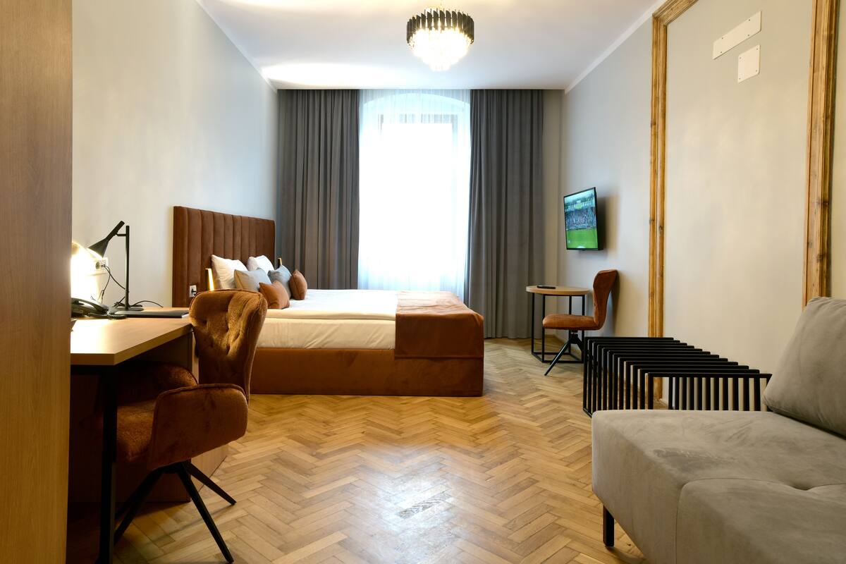 Une chambre d’hôtel équipée d’un lit, d’un bureau, d’une chaise, d’un canapé, d’une télévision et d’une fenêtre avec des rideaux.