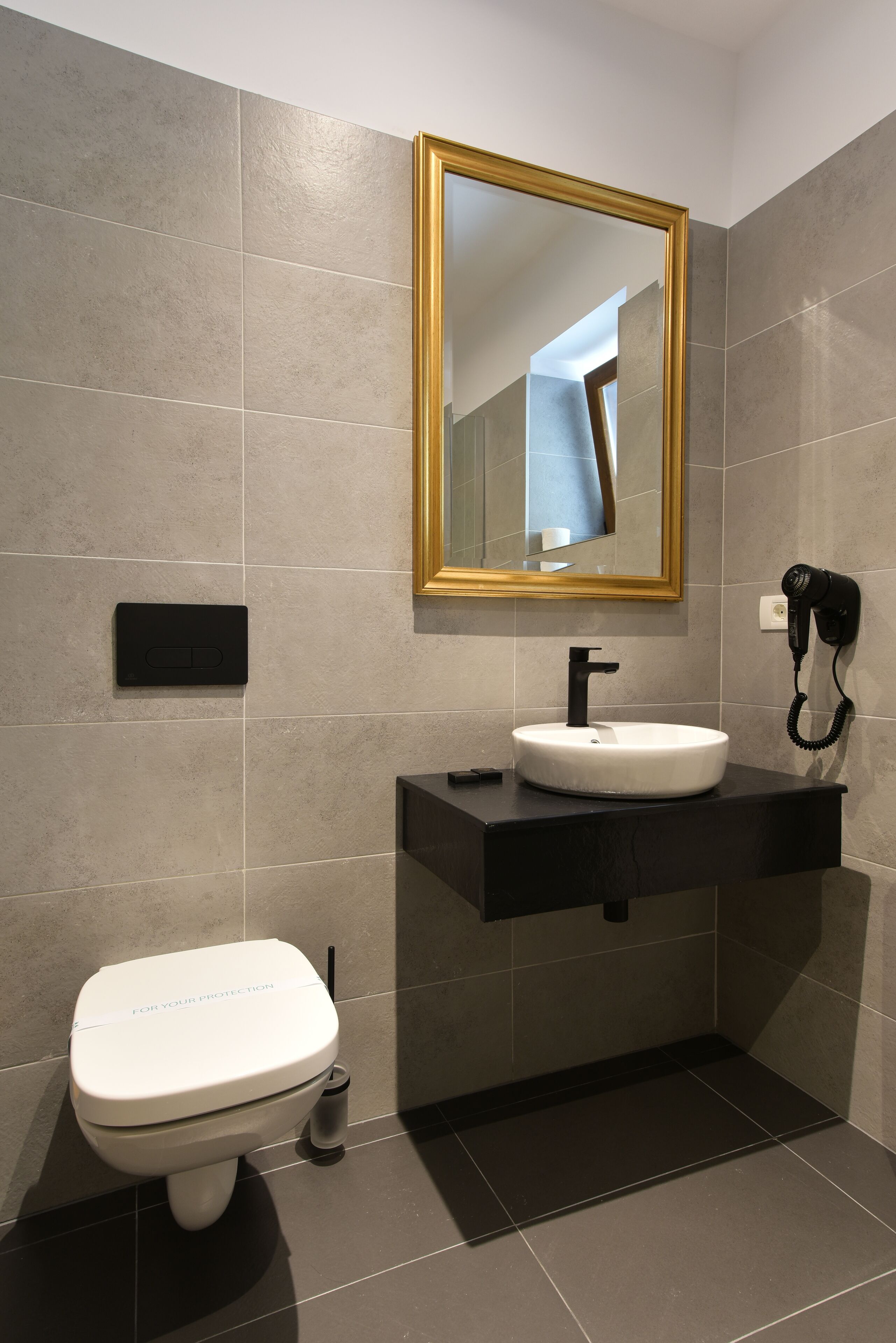 Een moderne badkamer met een wit toilet, een zwart wastafel en een spiegel met gouden lijst.