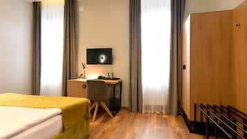 A hotel room with a bed, a desk, a chair, a TV, and a wardrobe.