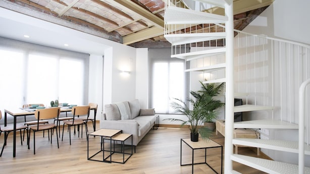 Un interior moderno con zona de comedor, un sofá, una escalera y una planta en maceta.