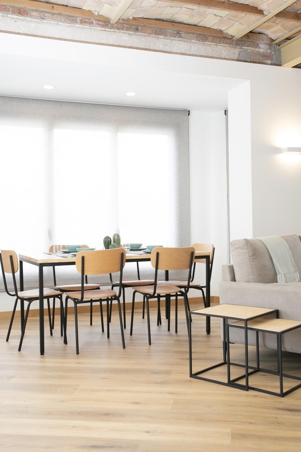 A dining area with a wooden table and chairs, a sofa, and a large window with curtains.