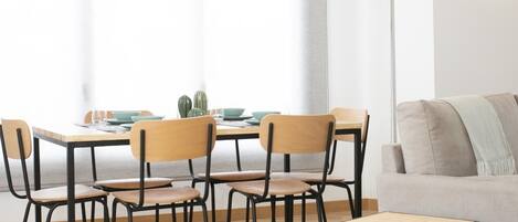 A dining area with a wooden table and chairs, a sofa, and a large window with curtains.