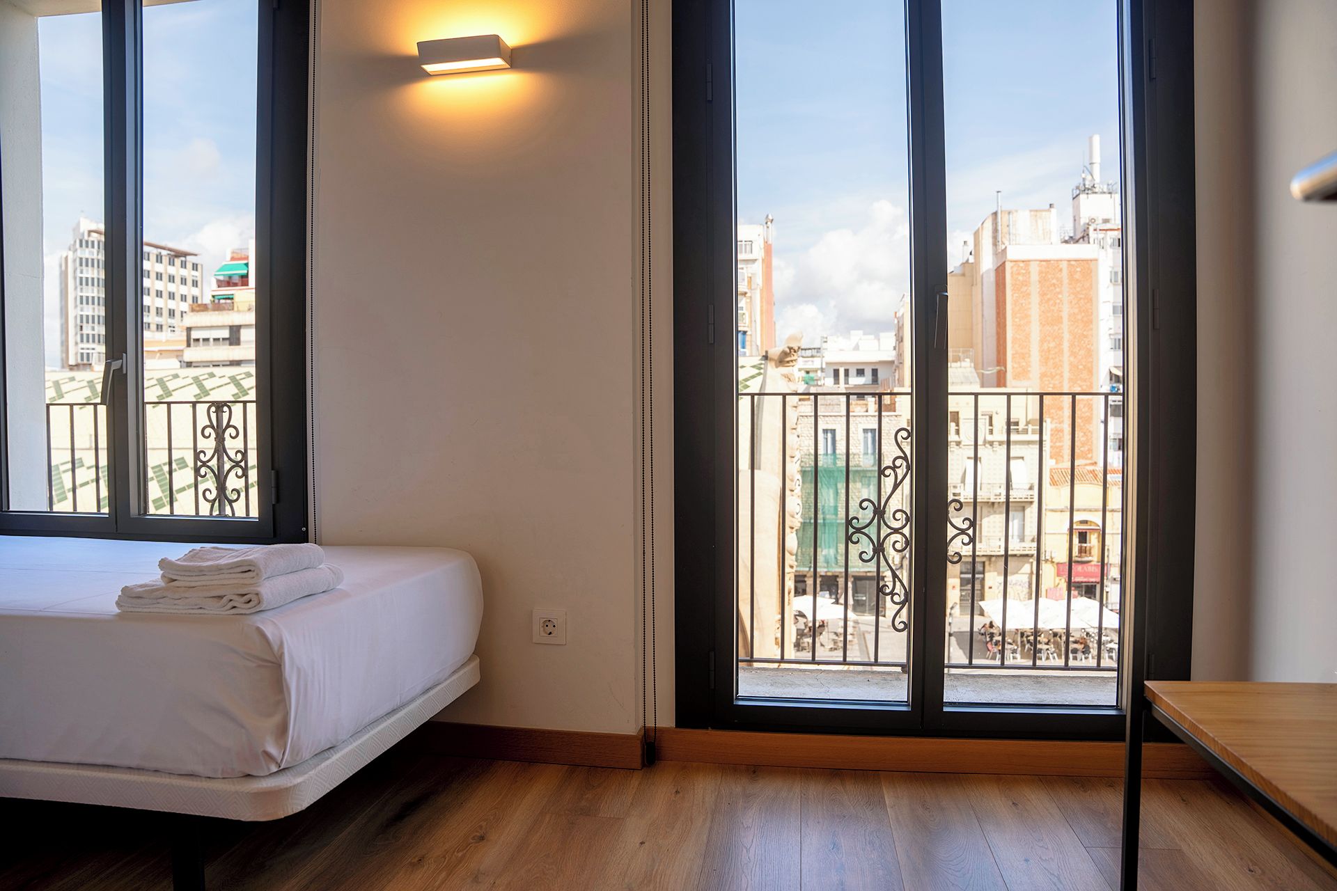 Une chambre d’hôtel avec un lit, un plancher en bois, un balcon doté d’une rambarde en métal et une vue sur la ville.