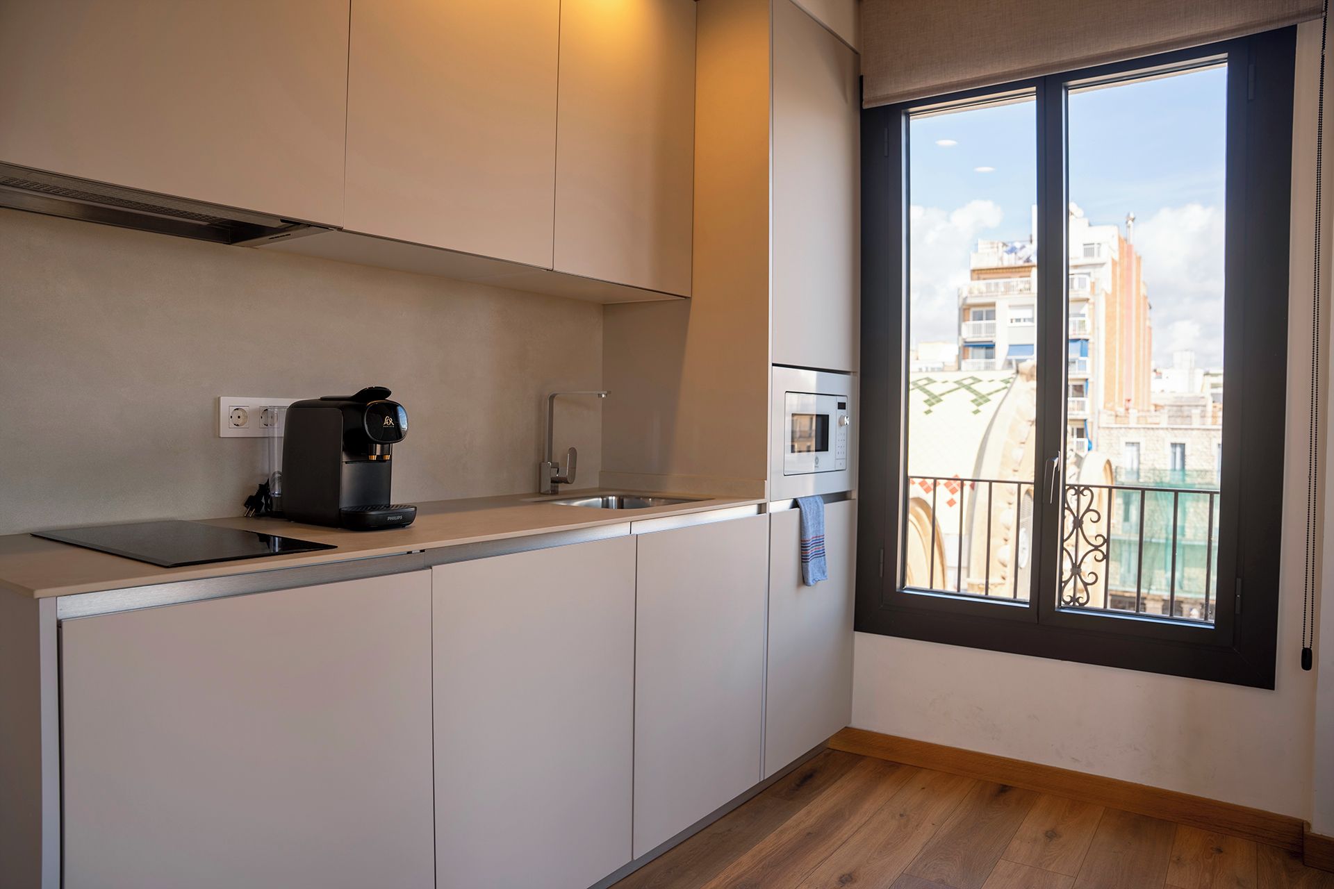 A modern kitchen with a coffee maker, microwave, and a view of the city through a balcony door.