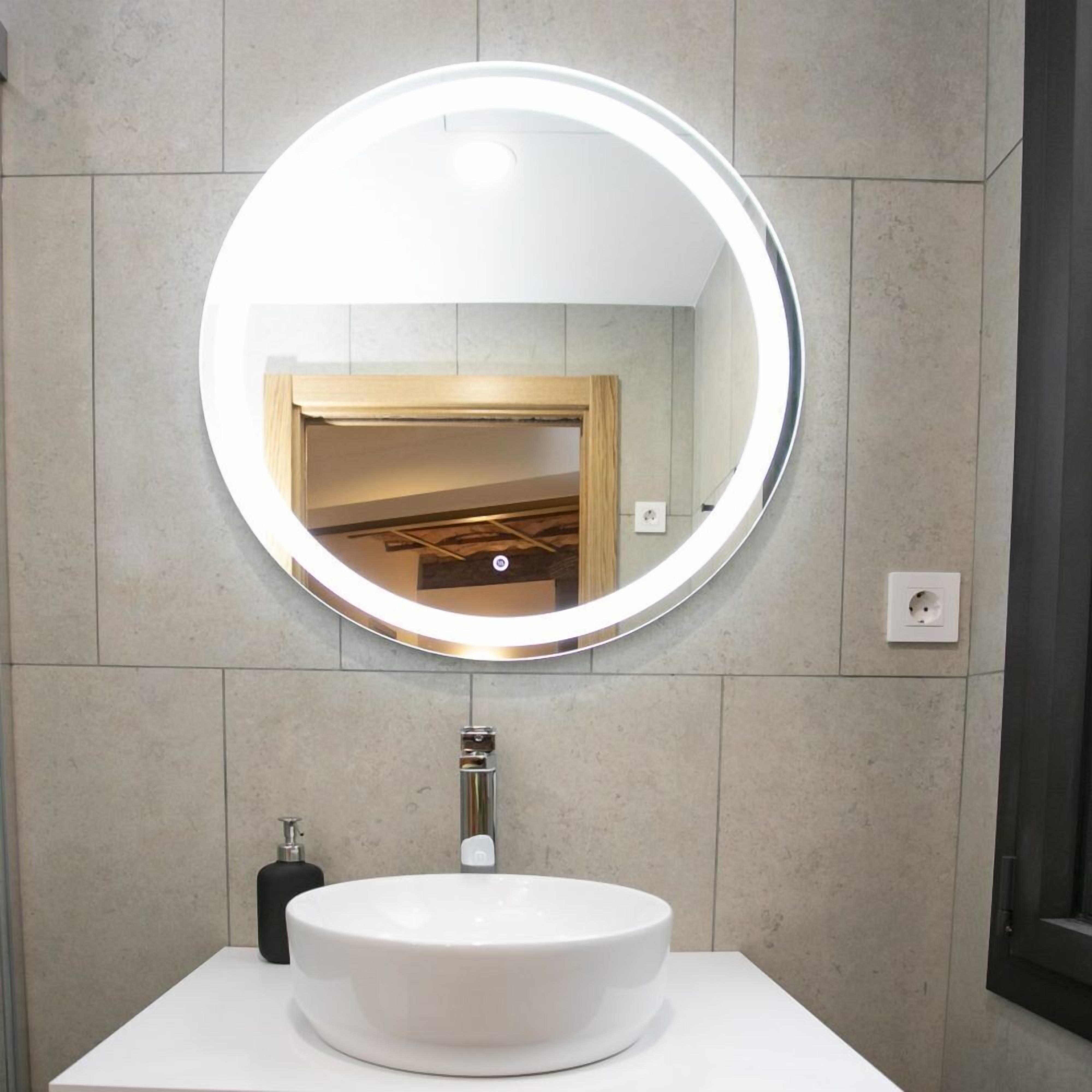 A bathroom with a round mirror, a white sink, and a towel dispenser.