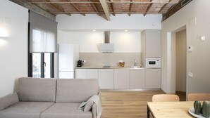 Una sala de estar moderna con un sofá, una mesa de comedor y una cocina con armarios y electrodomésticos blancos.