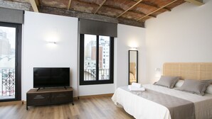 Un dormitorio con cama, televisor, cómoda y ventana con vista a la ciudad.
