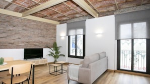 Una sala de estar moderna con pared de ladrillo, suelo de madera, un sofá gris, un televisor y un área de comedor con una mesa y sillas.