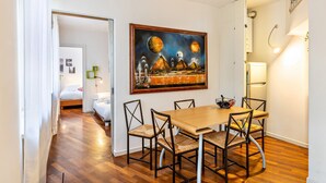 Un coin repas avec une table et des chaises en bois, un tableau au mur et un lit dans la pièce adjacente.