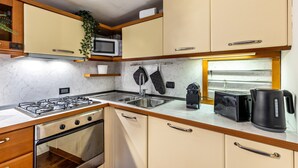 Une cuisine compacte équipée d’une cuisinière à gaz, d’un four à micro-ondes, d’un grille-pain, d’une bouilloire et de meubles de rangement en bois.