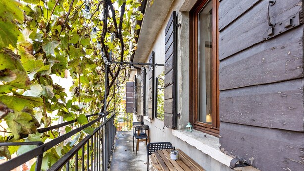 Un balcon avec une table et des chaises en bois, une rambarde en métal et un bâtiment doté d’une fenêtre et d’une porte.