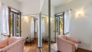 Une chambre moderne avec un plancher en bois, un grand miroir, deux fauteuils roses et une petite table sur laquelle est posée une bougie.
