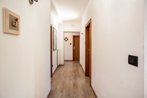 Ein schmaler Korridor mit Holzdielen, weißen Wänden und einer Tür am Ende.