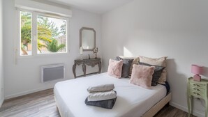 Un dormitorio con cama, mesita de noche, espejo y ventana con vistas a zonas verdes.