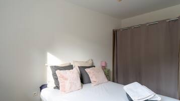 A bedroom with a bed, pillows, a nightstand, a lamp, and a curtain.