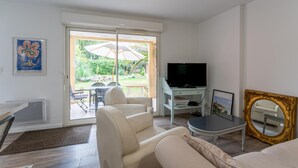 Una sala de estar con televisor, sofá, mesa de centro y puerta corrediza de vidrio que da a un área exterior con mesa y sillas.