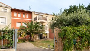 Un edificio residencial con entrada protegida por una reja, un patio con mobiliario exterior y una palmera.