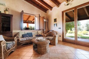 A cozy living area with wicker furniture, a tiled floor, and a large sliding glass door leading to an outdoor space.