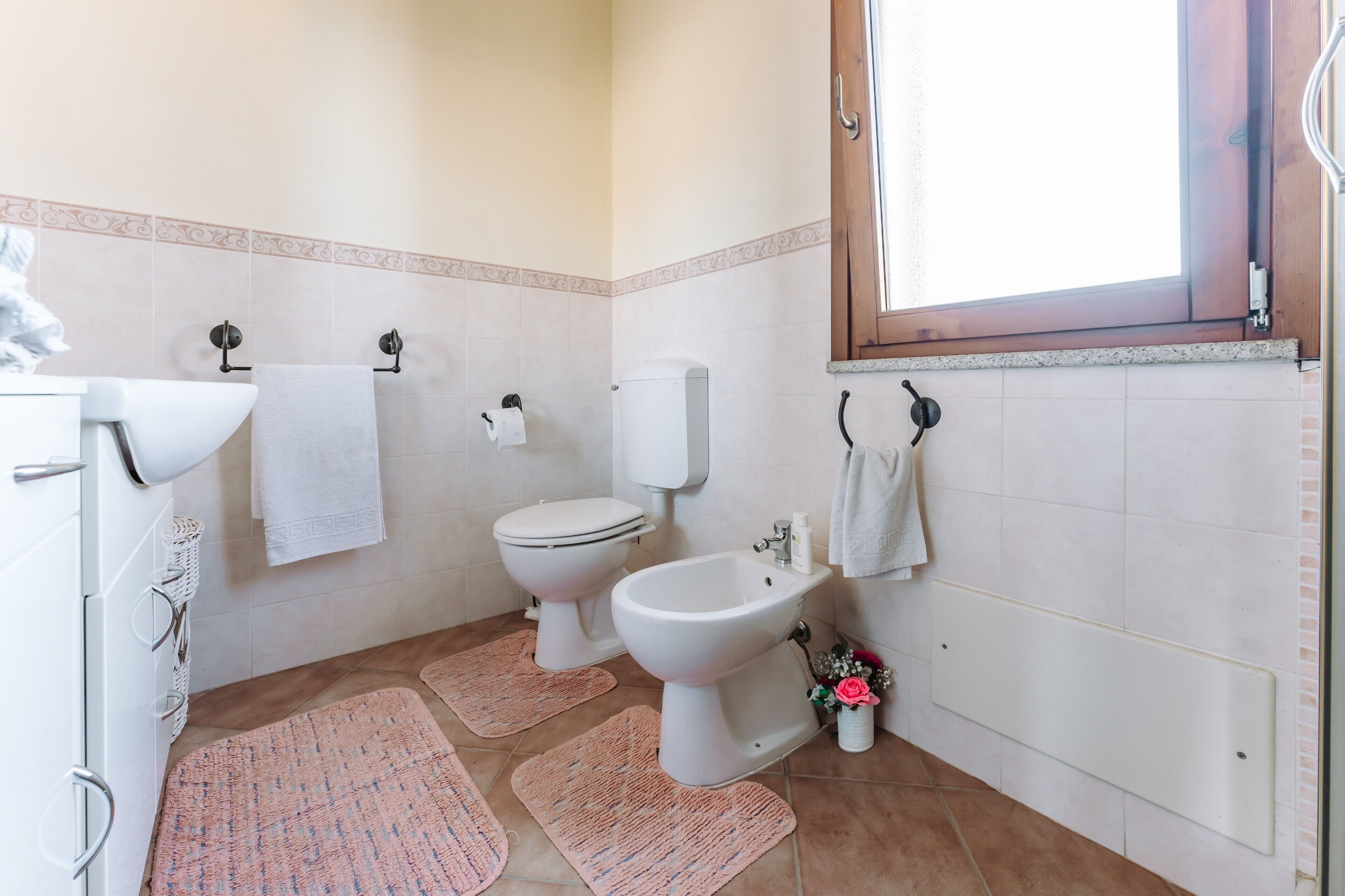 A bathroom with a toilet, bidet, sink, and a window.