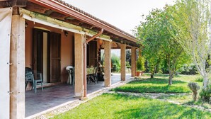 A covered outdoor area with a table and chairs, a door, and a garden with trees and grass. - Villa 'Casa Serra' with Mountain View, Wi-Fi and Air Conditioning (Pimentel)