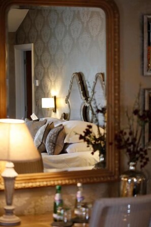 A bedroom with a large mirror, a bedside lamp, and a bed with pillows.