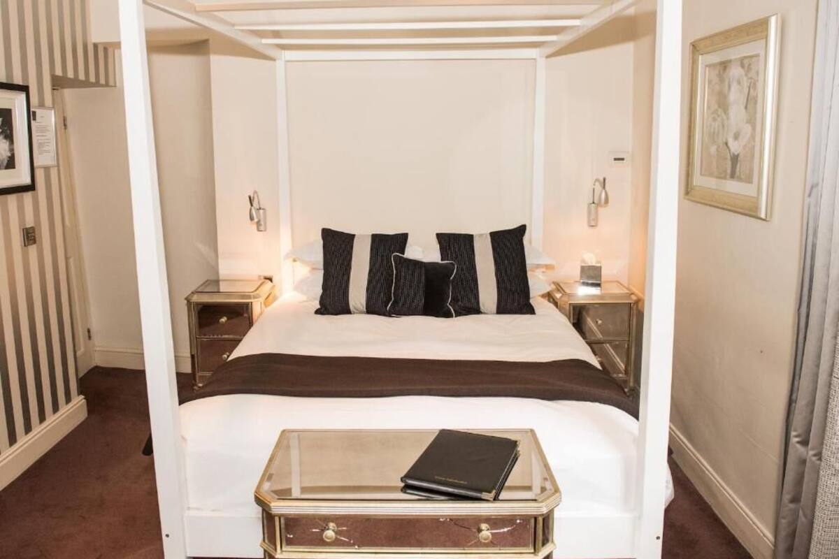 A four-poster bed with a glass bedside table, black and white bedding, and two bedside lamps.