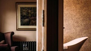 Um quarto com uma poltrona antiga, um quadro emoldurado na parede e uma banheira moderna.