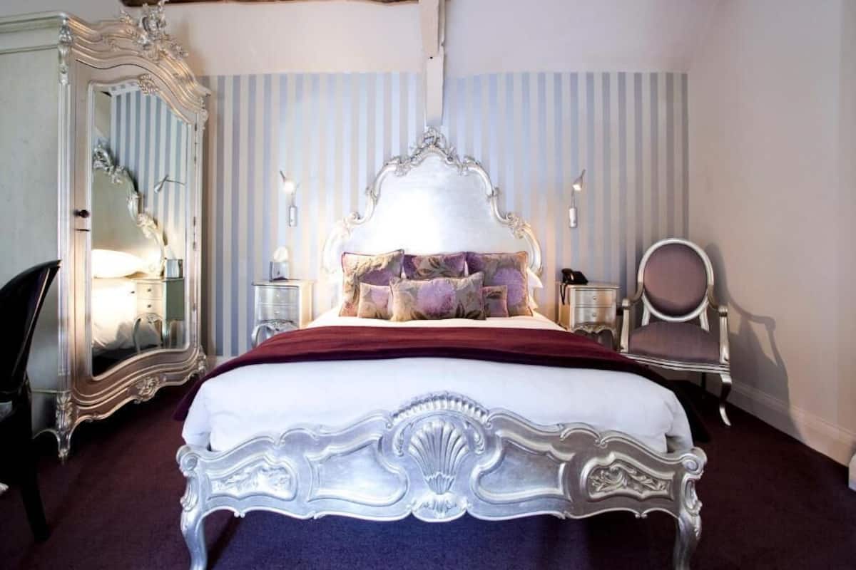 A bedroom with a large ornate bed, a mirror, a chair, and a nightstand.