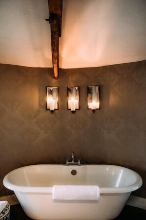 A bathroom with a freestanding bathtub, three wall-mounted sconces, and a wooden beam above the tub.
