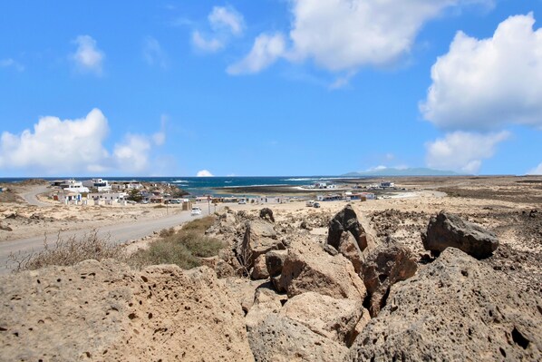 A coastal landscape with rocky terrain, a road, and a cluster of buildings. - Holiday home 'Casa Vicente Majanicho' with shared pool, private terrace and Wi-Fi (lajares)