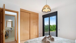 Une chambre avec un lit, un luminaire suspendu, une porte coulissante et une vue sur la verdure à l’extérieur.