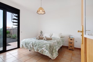 Une chambre avec un lit, un luminaire suspendu, une petite table de chevet en bois et une porte-fenêtre coulissante donnant sur un espace extérieur.
