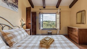 Un dormitorio con una cama, un aparador de madera, una ventana con una persiana abierta y un cuadro en la pared.