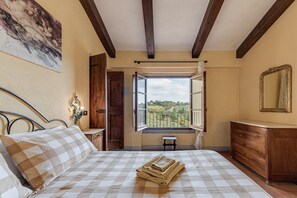 Um quarto com uma cama, uma cômoda de madeira, uma janela com uma persiana aberta e um quadro na parede.