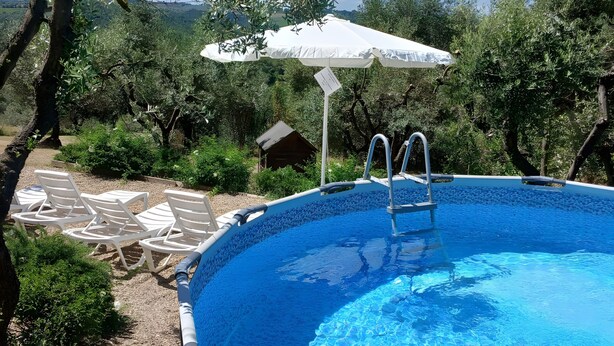 Una piscina con escalera, rodeada de sillas de descanso y una sombrilla.