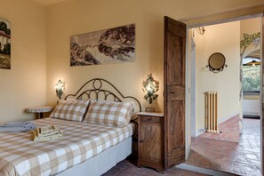 A bedroom with a bed, a nightstand, a wooden wardrobe, a wall-mounted mirror, and a radiator.