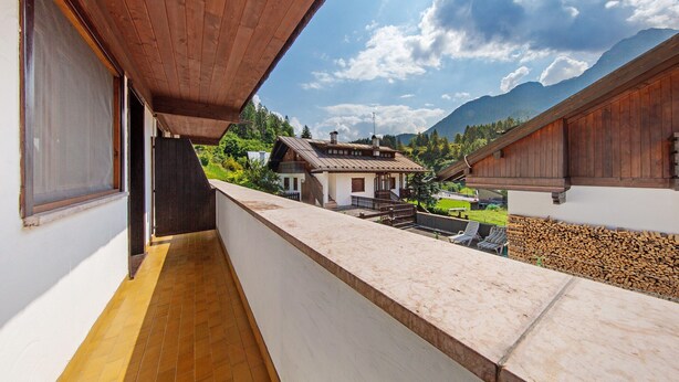 Un balcon donnant sur une montagne, un bâtiment en bois et un mur blanc.