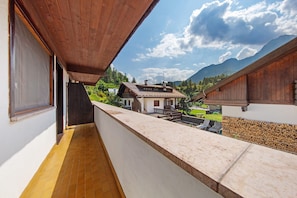 A balcony with a view of a mountain, a wooden building, and a white wall.