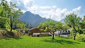 Un paysage rural avec une maison, un champ verdoyant et des montagnes en arrière-plan.