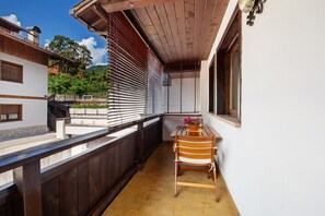Ein Balkon mit einem Holzstuhl, einem Tisch mit Blumenvase und Blick auf einen Garten und Gebäude.