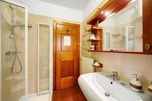 Een badkamer met een douche, een wastafel, een spiegel en een houten deur.
