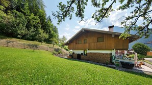 Une maison en bois avec un toit en pente, entourée d’une pelouse bien entretenue et d’arbres.
