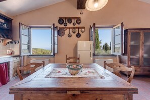 A rustic kitchen with a wooden table, chairs, and a view through large windows.
