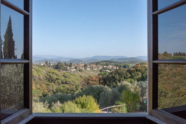 A view through a window of a town surrounded by hills and trees.
