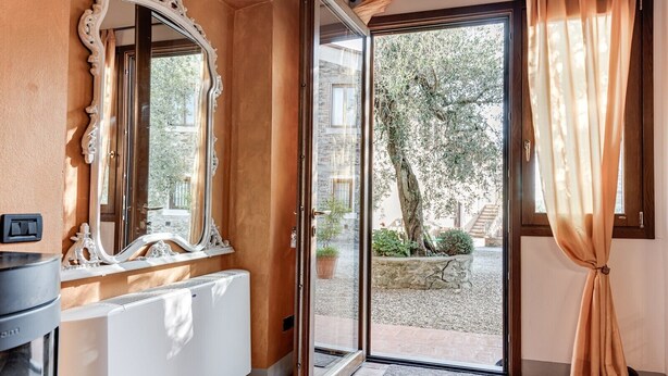A room with a large mirror, a radiator, a door leading outside, and a view of a garden. - Farmhouse 'Il Pintello - Lo Scricciolo' with Shared Pool, Wi-Fi and Air Conditioning (San Casciano VP)