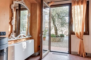 A room with a large mirror, a radiator, a door leading outside, and a view of a garden. - Farmhouse 'Il Pintello - Lo Scricciolo' with Shared Pool, Wi-Fi and Air Conditioning (San Casciano VP)