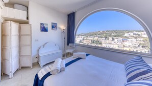 Una camera d'hotel con un letto, un armadio, una scrivania, una sedia e un'ampia finestra con vista sulla città.