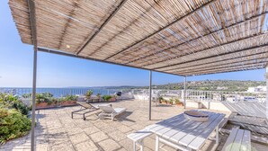 Una terrazza esterna con vista sul mare, arredata con tavoli e sedie e circondata da piante in vaso.
