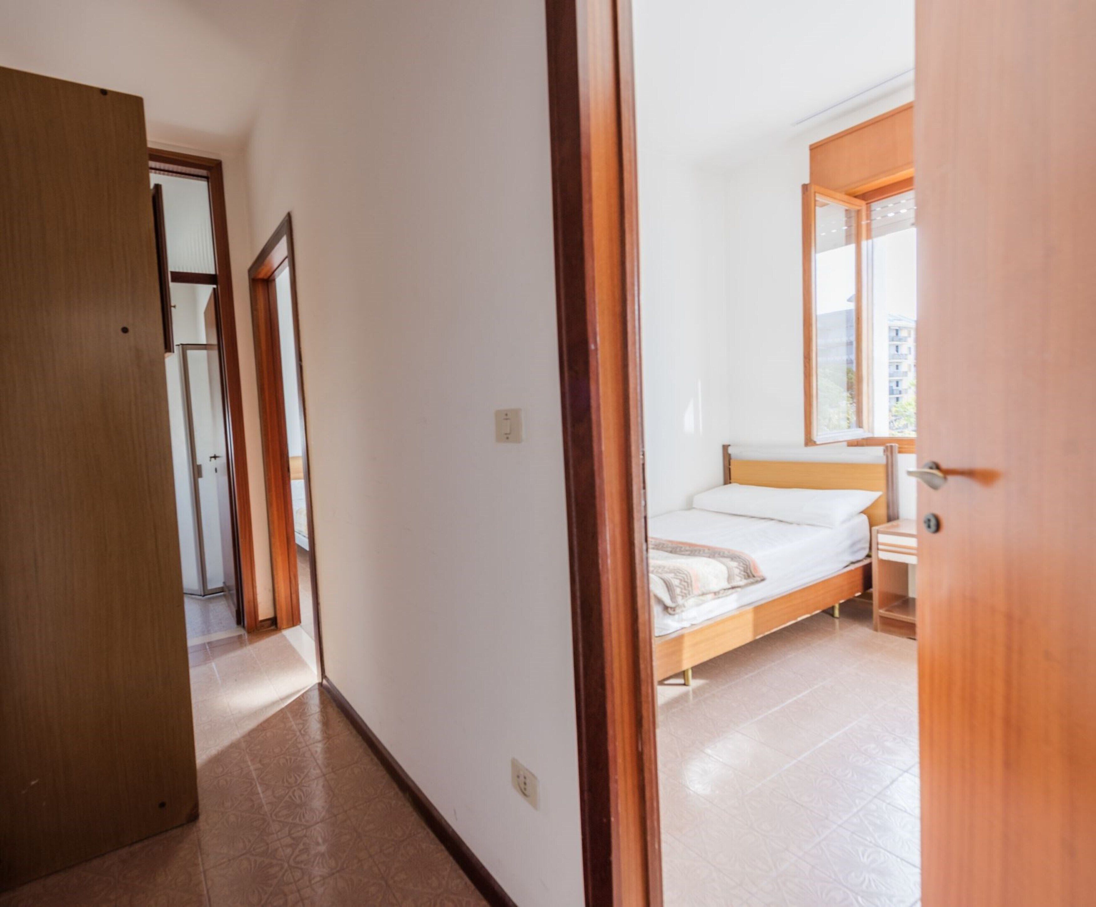 Ein Schlafzimmer mit Bett, Fenster und einer Tür zu einem anderen Raum.